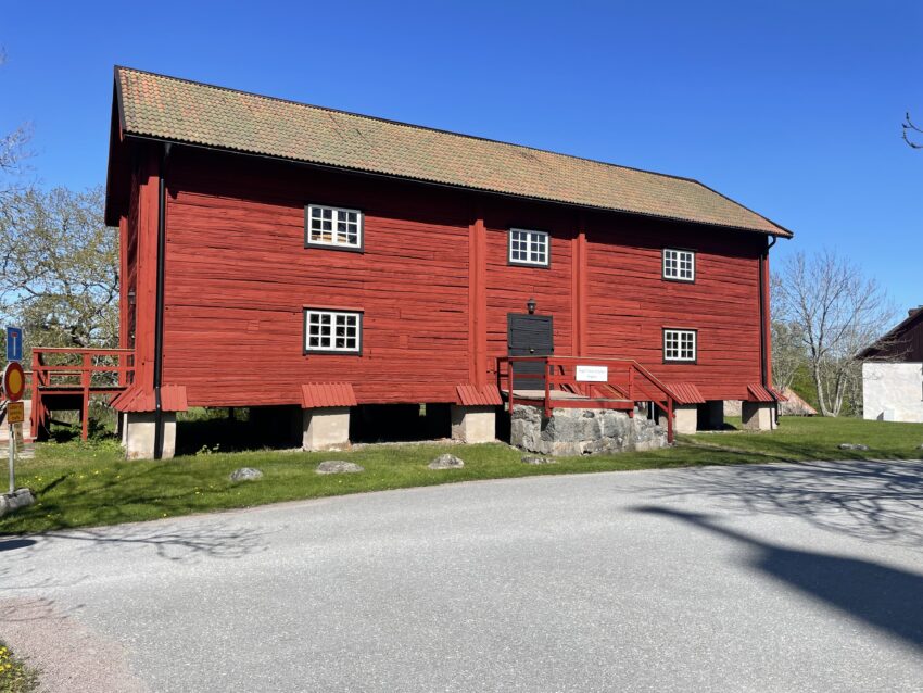 Bilden visar framsidan på Magasinet som är Engsö hembygdsförenings hembygdsmuseum. Magasinet är målat i falurödfärg, står på plingar och har en ingång mitt på långsidan.