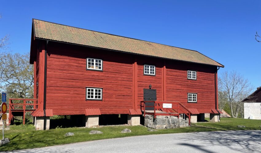 Bilden visar framsidan på Magasinet som är Engsö hembygdsförenings hembygdsmuseum. Magasinet är målat i falurödfärg, står på plingar och har en ingång mitt på långsidan.